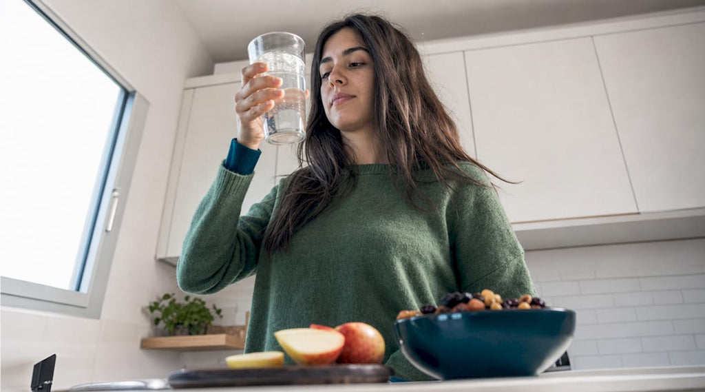 Een vrouw zit aan de eettafel en neemt een slok van haar sportdrank met elektrolyten.