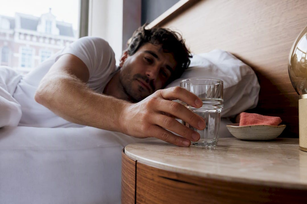 Hand grijpt naar waterglas naast het bed