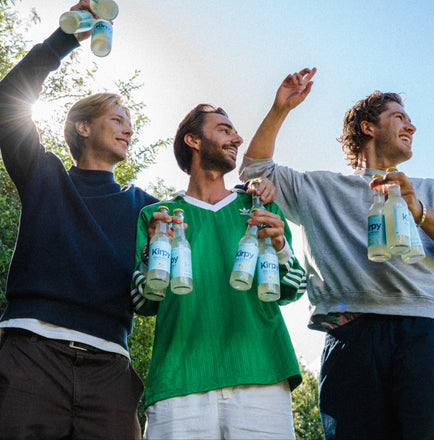 founders kirpy  standing outdoors, holding bottles and smiling.
